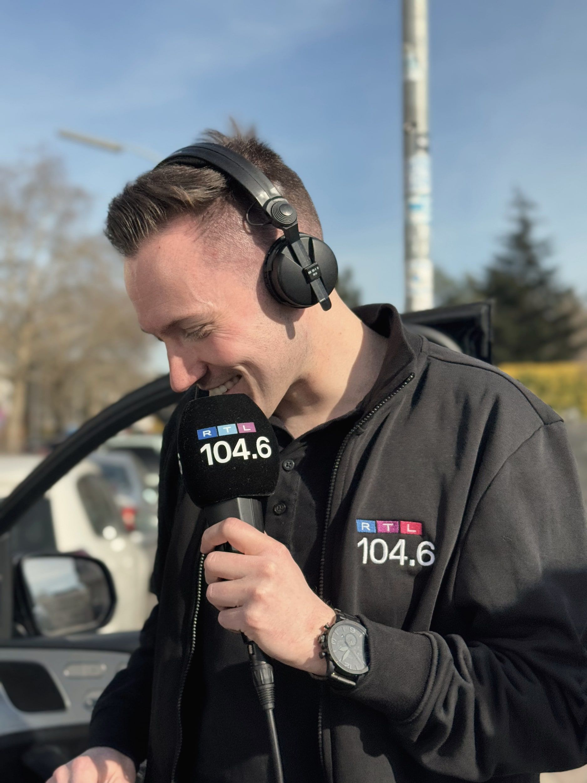 Chris Hartmann mit Kopfhörern und Mikrofon von 104.6 RTL bei einer Außenreportage